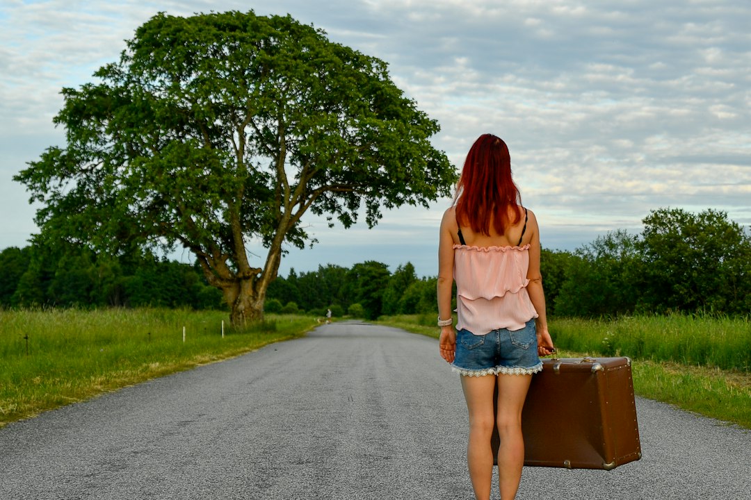 Mujer con maleta en una carretera rural; imagen ilustrativa de un viaje